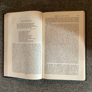 May include: An open book with a tan leather cover and yellowed pages. The book is titled "Essays: First Series" and the text on the page discusses the concept of the "Over-Soul".