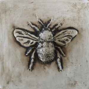 May include: A ceramic tile with a raised image of a bumblebee. The bumblebee is in shades of brown and white and has detailed wings.