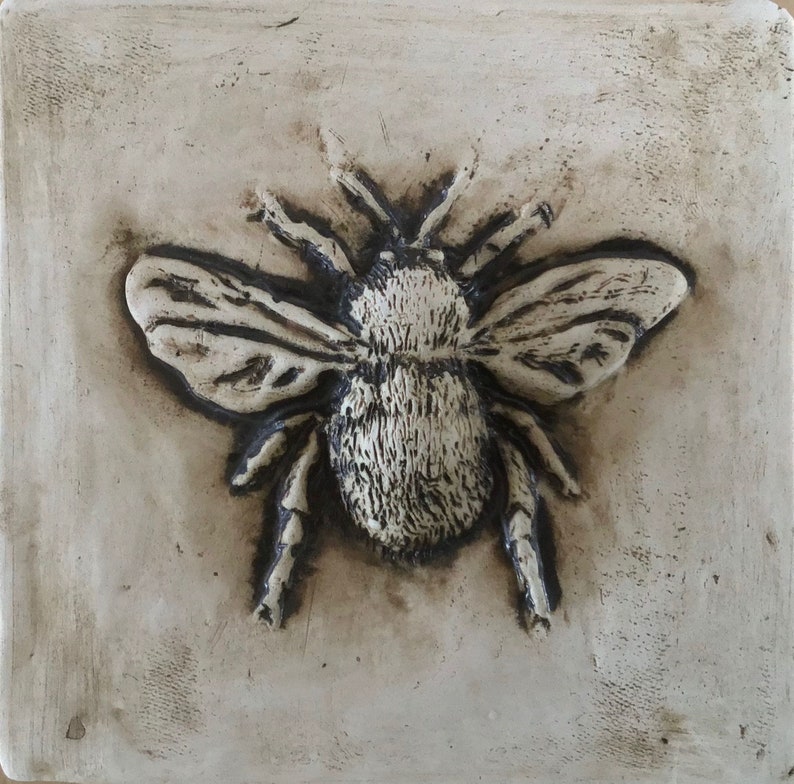 May include: A ceramic tile with a raised image of a bumblebee. The bumblebee is in shades of brown and white and has detailed wings.