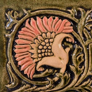 May include: A ceramic tile with a floral design. The tile is green with a pink flower and brown accents.