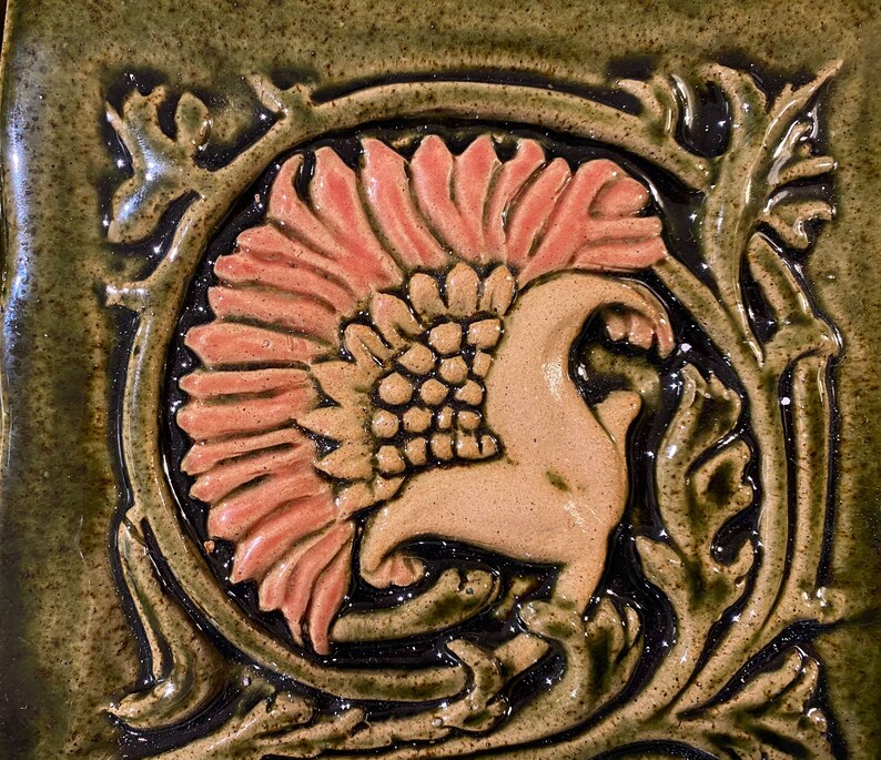 May include: A ceramic tile with a floral design. The tile is green with a pink flower and brown accents.