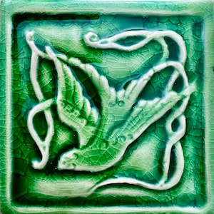 May include: A green ceramic tile with a white raised design of a bird in flight. The tile has a crackled glaze.