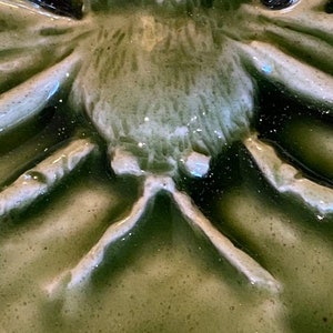 May include: Close-up of a green ceramic spider with white accents. The spider has a detailed, textured body and legs.