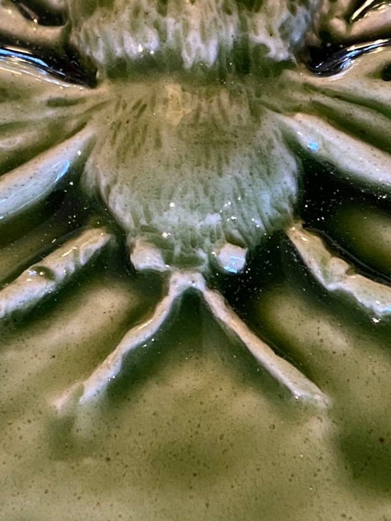 May include: Close-up of a green ceramic spider with white accents. The spider has a detailed, textured body and legs.