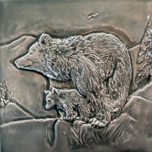 May include: A ceramic tile with a raised relief design of a mother bear and her cub. The bear and cub are in a natural setting with a green background.
