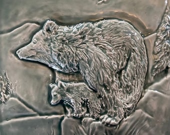 May include: A ceramic tile with a raised relief design of a mother bear and her cub. The bear and cub are in a natural setting with a green background.