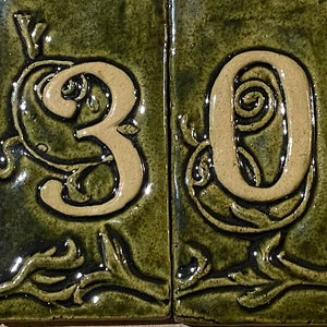 May include: A set of five ceramic tiles with a green background and white numbers. The numbers are 2309. Each tile has a floral design around the number.