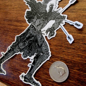 K&ouml;nnte beinhalten: Schwarz-wei&szlig;er Aufkleber mit einer detaillierten Illustration einer Figur, die von Pfeilen durchbohrt wird. Die Figur befindet sich in einer dynamischen Pose, mit komplizierten Mustern auf ihrer Kleidung. Eine kanadische 5-Cent-M&uuml;nze befindet sich neben dem Aufkleber.