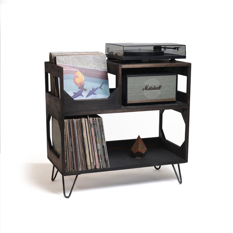 May include: A dark stained wooden record player stand with a turntable, speaker, and vinyl records. The stand has three shelves, with a speaker on the middle shelf and records on the top and bottom shelves. The stand has black metal hairpin legs.