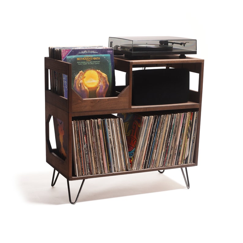 May include: A wooden record player stand with a turntable on top and storage for vinyl records. The stand is dark brown with black metal legs. The stand has multiple compartments for record storage and a shelf for the turntable.