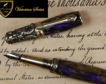 Può includere: Una penna stilografica con fusto e cappuccio marmorizzati viola e oro. Il cappuccio presenta dettagli in metallo color bronzo scuro con motivi floreali e una clip abbinata. Il pennino è in metallo argentato. Il testo Provincial Mills Victorian Series è visibile.