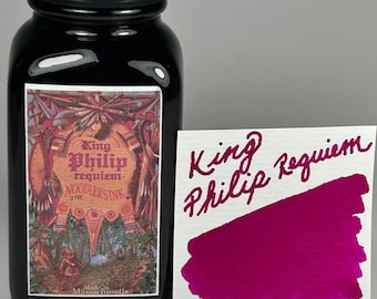 Può includere: Un flacone in vetro da 89 ml di Noodler's Ink con tappo nero e un'etichetta con il testo King Philip-requiem-NOODLER'S INK. Accanto al flacone c'è un cartoncino bianco con il testo King Philip Requiem scritto in inchiostro magenta su una macchia.