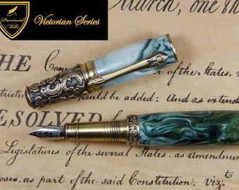 Pode incluir: Uma caneta-tinteiro com corpo e tampa em resina marmoreada verde e branca, apresentando detalhes em metal tom latão antigo com gravações ornamentais. A tampa inclui um clipe de metal e a pena é de metal prateado.