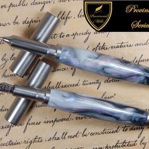 May include: Two pens with metallic caps and bodies featuring a marbled pattern of white, gray, and purple swirls. One pen has a visible metal nib, while the other is capped. A black logo in the corner reads Provincial Mills Provincial Series.