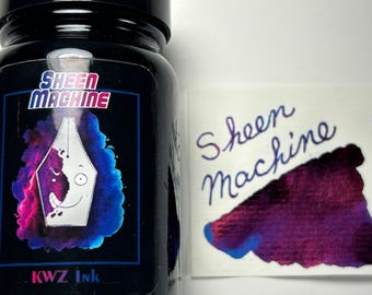 Può includere: Una bottiglia di vetro nero di inchiostro KWZ etichettata Sheen Machine con il disegno di un pennino stilografico circondato da nuvole di inchiostro blu e magenta. Accanto alla bottiglia c'è un campione di carta bianca con il testo Sheen Machine.