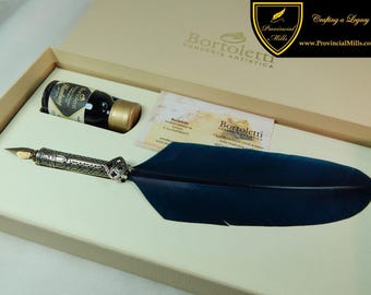 May include: A dark blue quill pen with an ornate silver-toned metal handle and a gold-toned nib, presented in a beige box alongside a small glass bottle of ink and a rectangular informational card featuring the Bortoletti Fonderia Artistica logo.
