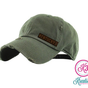 May include: A green distressed baseball cap with a brown leather patch that says "Kentucky" on it.