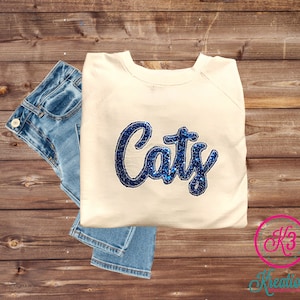 May include: A cream-colored sweatshirt with the name "Caty" spelled out in blue glitter letters.