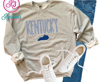 May include: A gray sweatshirt with a blue and white gingham pattern spelling "Kentucky" and a blue outline of the state of Kentucky.