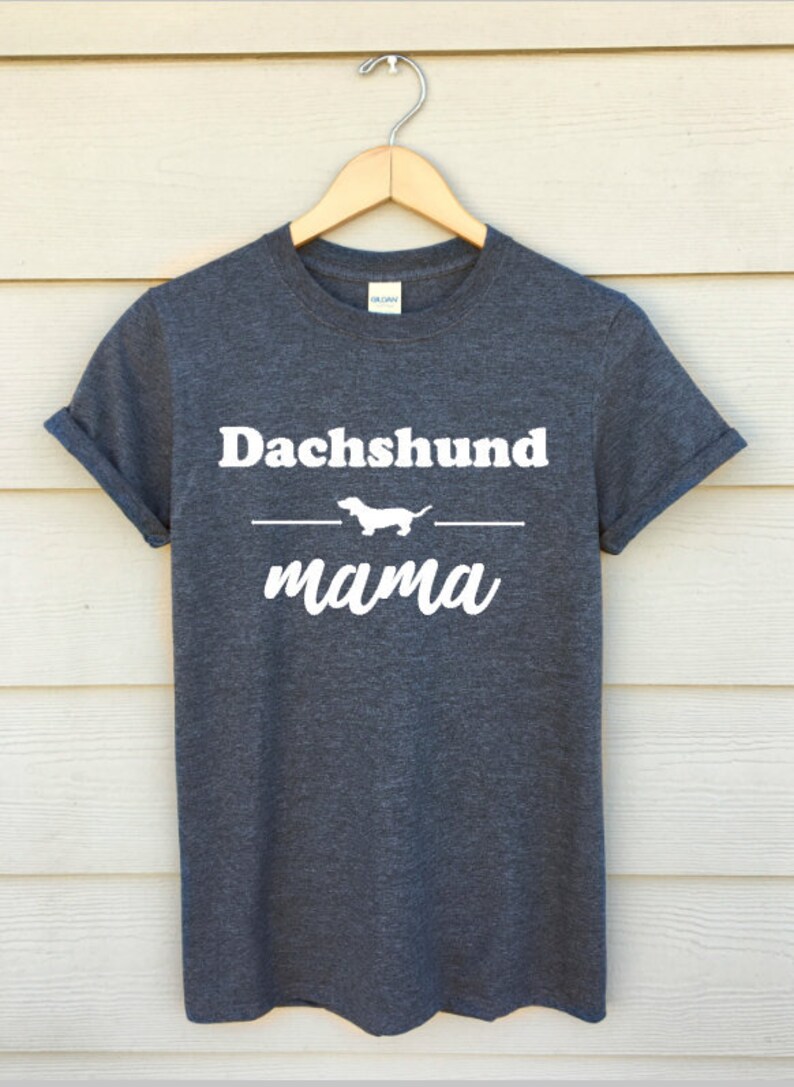Peut inclure: Un t-shirt gris fonc&eacute; avec le texte "Dachshund mama" en blanc. Une silhouette blanche de dachshund est au-dessus du mot "mama".