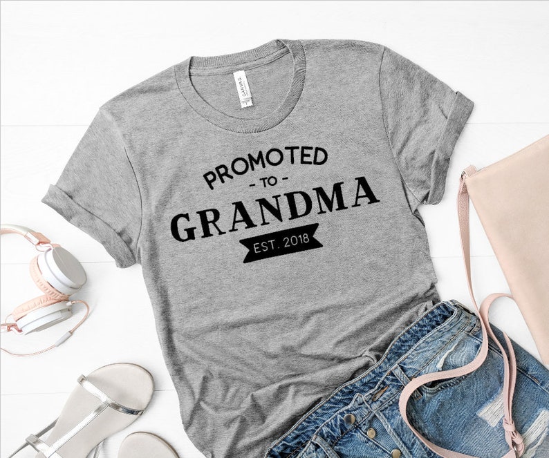 May include: Gray t-shirt with black text that reads "Promoted to Grandma Est. 2018".