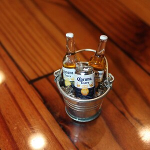 May include: A silver bucket filled with ice and three bottles of Corona Extra beer. The bottles are chilled and ready to be enjoyed.