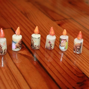 May include: Six miniature candles with orange flames and images of dogs on the sides. The candles are arranged in a row on a wooden surface.