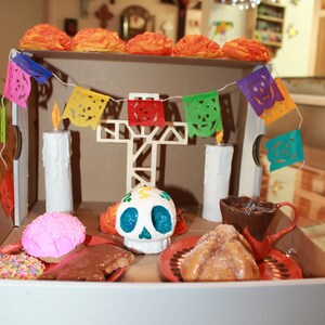 May include: A Day of the Dead altar with a sugar skull, candles, and traditional Mexican treats. The altar is decorated with colorful paper flags and flowers.