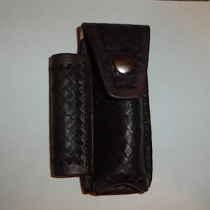 May include: A brown leather case with a snap closure. The case has a woven pattern and is designed to hold a small object.