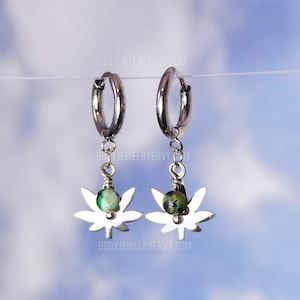 May include: A pair of silver hoop earrings with a dangling green stone and a silver marijuana leaf charm.