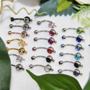 May include: A collection of curved barbell body jewelry pieces featuring various metal finishes including silver, gold, black, and iridescent tones. Each piece is adorned with a single round or square faceted gemstone in colors like pink, red, blue, green, and clear.