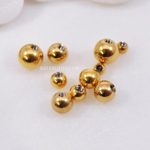 May include: A collection of gold-colored metal balls of various sizes. The balls have a threaded hole in the center.