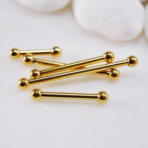 May include: A collection of gold-colored metal barbell body jewelry pieces. Each piece consists of a straight, smooth rod with a small, polished spherical ball attached to both ends. The items are arranged in a loose, overlapping pile.