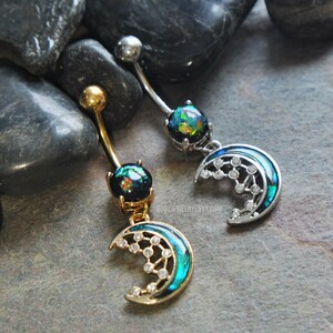 May include: Two belly button rings with a crescent moon charm. The charms are adorned with iridescent opal stones and clear rhinestones. One ring is gold-toned and the other is silver-toned.
