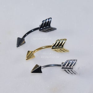 May include: Three curved barbell body jewelry pieces shaped like arrows, each featuring a pointed tip and a fletched end. The set includes one black, one gold-toned, and one silver-toned piece, all displaying the text BODYJEWELRYENVY.COM.