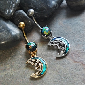 May include: Two belly button rings featuring a curved barbell with a round, iridescent dark stone at the top and a crescent moon charm at the bottom. One ring is gold-toned and the other is silver-toned, both with small clear stones on the moon.