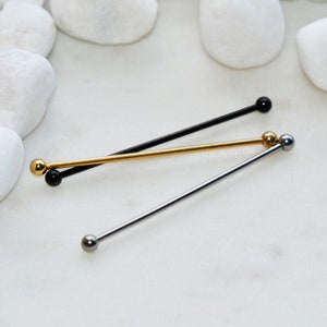 Könnte beinhalten: Drei gerade Industrial-Piercing-Stäbe in Schwarz, Gold und Silber. Jeder Stab besteht aus einem langen, dünnen Metallschaft mit einer kleinen, glatten, kugelförmigen Kugel an jedem Ende. Die Schmuckstücke sind in einem überlappenden Muster angeordnet.