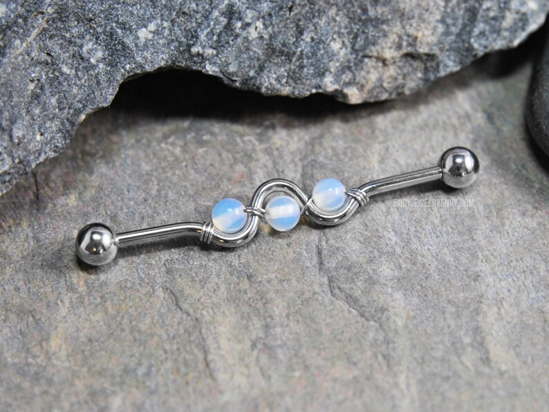 May include: A silver barbell with a wavy design and three white opal beads.