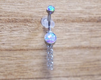 May include: A curved barbell belly ring featuring two round, iridescent opal-style stones set in silver-toned metal. The bottom stone is larger and attached to a short, dangling silver-toned chain. The text BODYJEWELRYENVY.COM is visible.