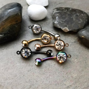 Puede incluir: Cinco piezas de joyer&iacute;a corporal tipo barra curva con cristales facetados transparentes. Los acabados met&aacute;licos incluyen plata, oro, oro rosa, negro y un tono arco&iacute;ris iridiscente. Cada pieza tiene un peque&ntilde;o aro y el texto BODYJEWELRYENVY.COM.
