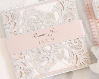 May include: A white envelope with a silver and pink laser cut wedding invitation with the text "Brianna y Jose 05.25.19".