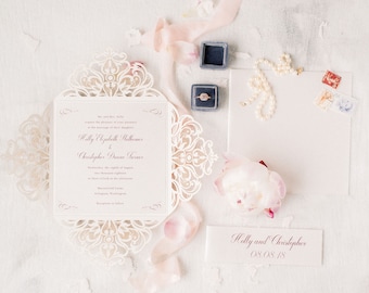 May include: A white wedding invitation with a delicate lace design. The invitation features the names "Holly Elizabeth Matthews" and "Christopher Duane Turner" in burgundy script. The date of the wedding is August 8th, 2018.
