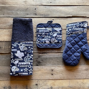 May include: A set of three kitchen towels featuring a navy blue background with a white pattern of stars, footballs, and the words "Cowboys" and "Texas".