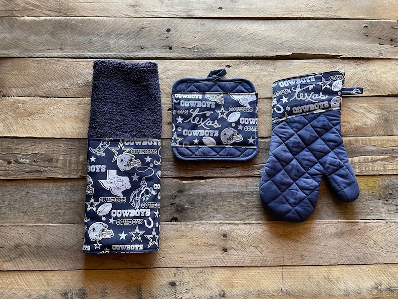 May include: A set of three kitchen towels featuring a navy blue background with a white pattern of stars, footballs, and the words "Cowboys" and "Texas".