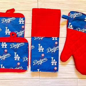 May include: Set of four red and blue kitchen pot holders with a Los Angeles Dodgers theme. The pot holders feature a baseball and the team's logo. The set includes two square pot holders, one oven mitt, and one rectangular towel.