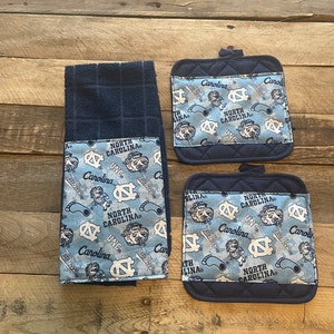 Pode incluir: Conjunto de tr&ecirc;s toalhas de cozinha azuis e brancas com tema North Carolina Tar Heels. As toalhas apresentam um padr&atilde;o repetido do logotipo dos Tar Heels, as palavras "North Carolina" e o mascote, Rameses. As toalhas s&atilde;o feitas de um tecido macio e absorvente e s&atilde;o perfeitas para secar pratos, m&atilde;os e derramamentos.