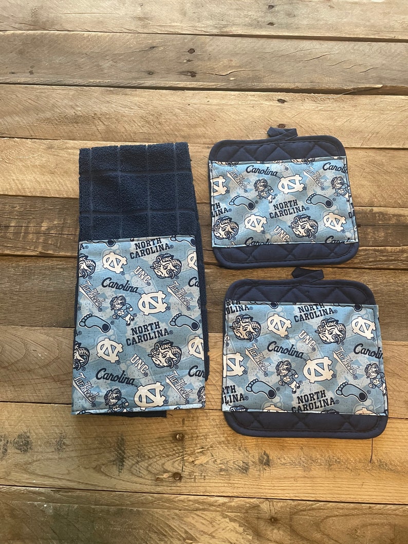Pode incluir: Conjunto de tr&ecirc;s toalhas de cozinha azuis e brancas com tema North Carolina Tar Heels. As toalhas apresentam um padr&atilde;o repetido do logotipo dos Tar Heels, as palavras "North Carolina" e o mascote, Rameses. As toalhas s&atilde;o feitas de um tecido macio e absorvente e s&atilde;o perfeitas para secar pratos, m&atilde;os e derramamentos.