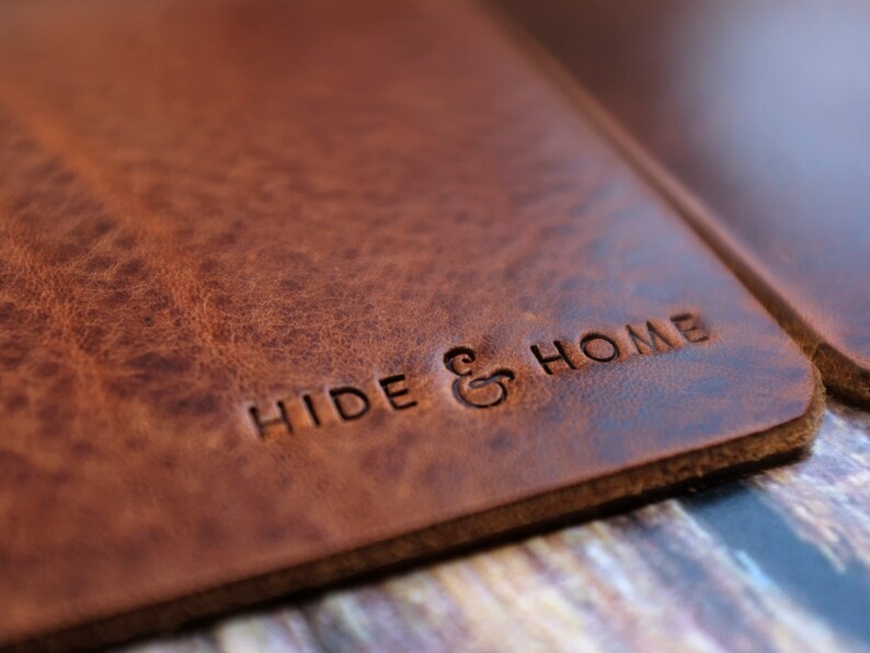 May include: Close-up of a brown leather product with the embossed text "HIDE & HOME". The leather has a textured, distressed appearance. The product appears to be a notebook cover or a similar item.