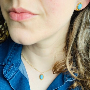 May include: A gold chain necklace with a blue oval pendant. The pendant has a gold border. The necklace is worn by a person with long brown hair.