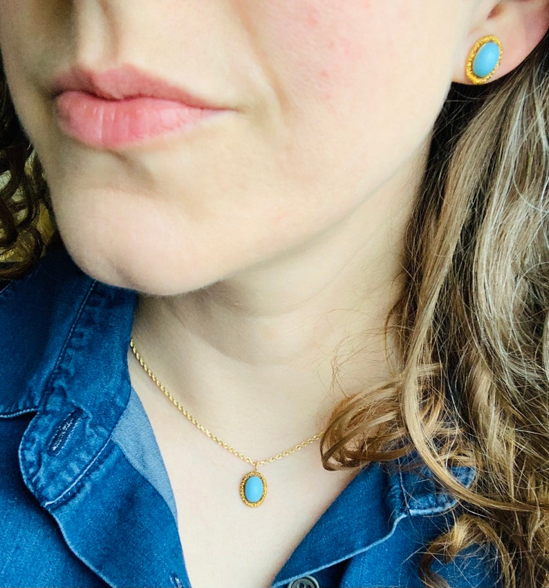 May include: A gold chain necklace with a blue oval pendant. The pendant has a gold border. The necklace is worn by a person with long brown hair.